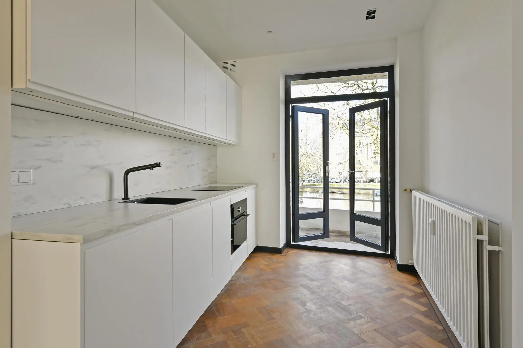 Moderne keuken aan de Cornelis Dopperkade met witte kasten, marmeren aanrechtblad en openslaande deuren naar een balkon met uitzicht op het water.